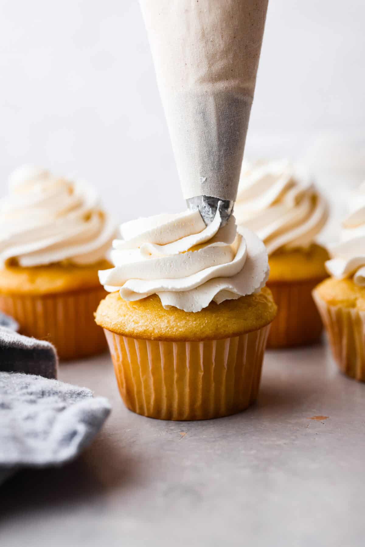 The most delicious Swiss Meringue Buttercream is easy to make with just 5 simple ingredients! It whips up deliciously light and silky with the right amount of sweetness. The perfect finishing touch for all of your favorite treats! Piping Swiss meringue buttercream onto a vanilla cupcake.
