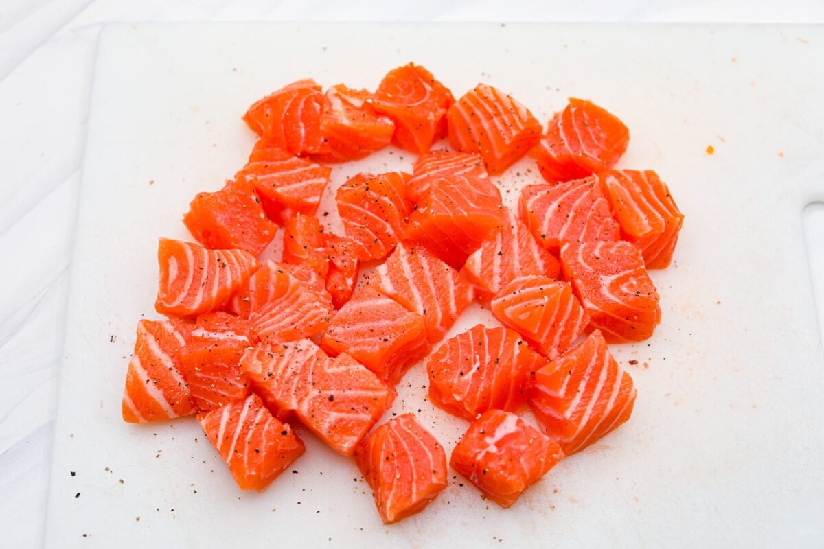 Cooked in less than 10 minutes, these perfectly glazed honey garlic air fryer salmon bites are so delicious. This is such a quick dinner, you will never want to cook salmon any other way! First photo of the salmon cut into bite-sized pieces. Second photo of the marinade mixed in a glass bowl. Third photo of the salmon marinating in the marinade. Fourth photo of the salmon bites lined in the air fryer before cooking.