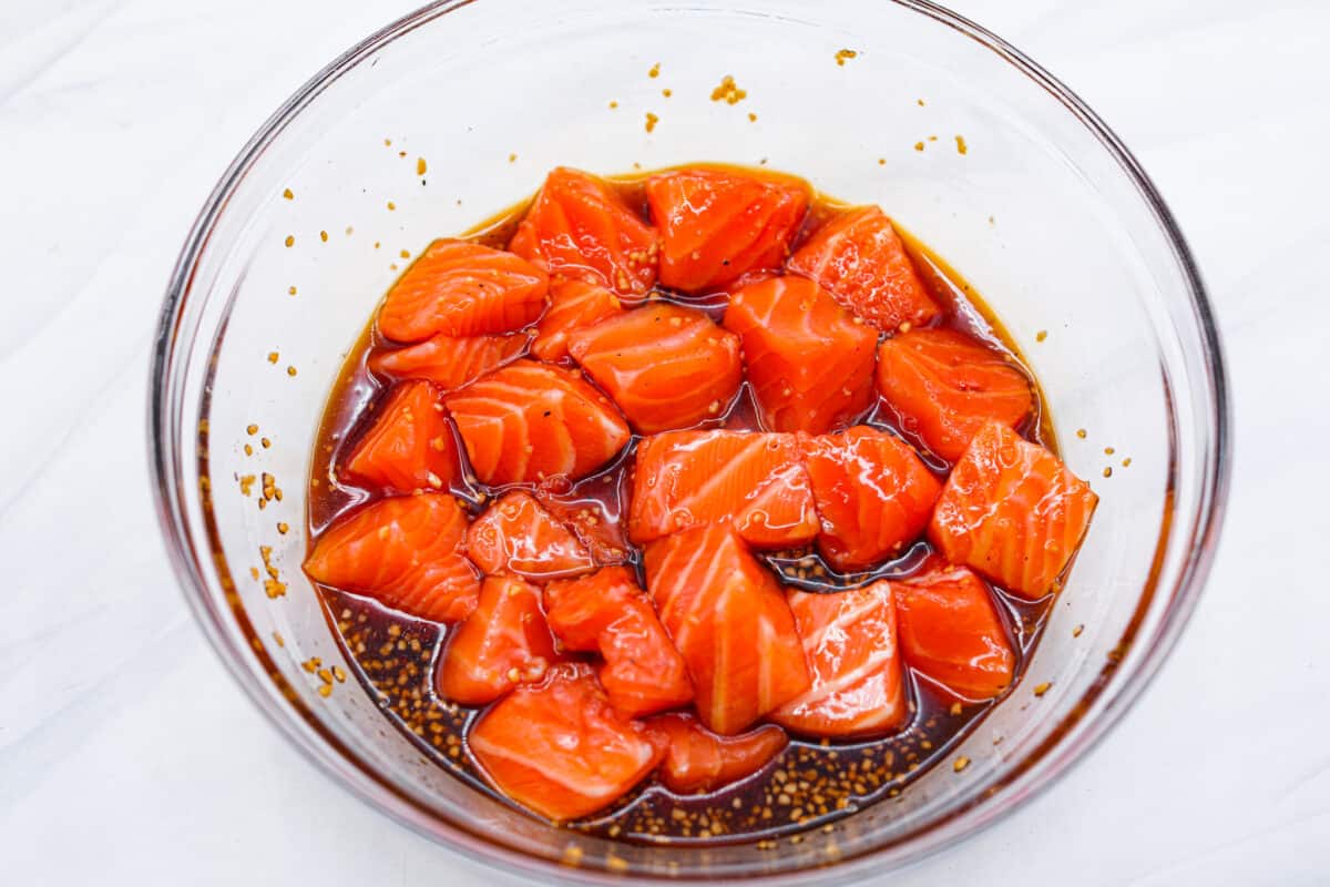 Cooked in less than 10 minutes, these perfectly glazed honey garlic air fryer salmon bites are so delicious. This is such a quick dinner, you will never want to cook salmon any other way! Salmon bites in a glass bowl with marinade.