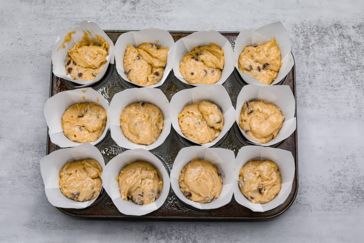 Treat yourself to these delicious Banana Chocolate Chip Muffins! With just a handful of ingredients and easy steps, you'll have moist and flavorful muffins ready to enjoy for breakfast (or to snack on!) in no time. Chocolate chip muffin batter in a muffin tin filled with white muffin liners.