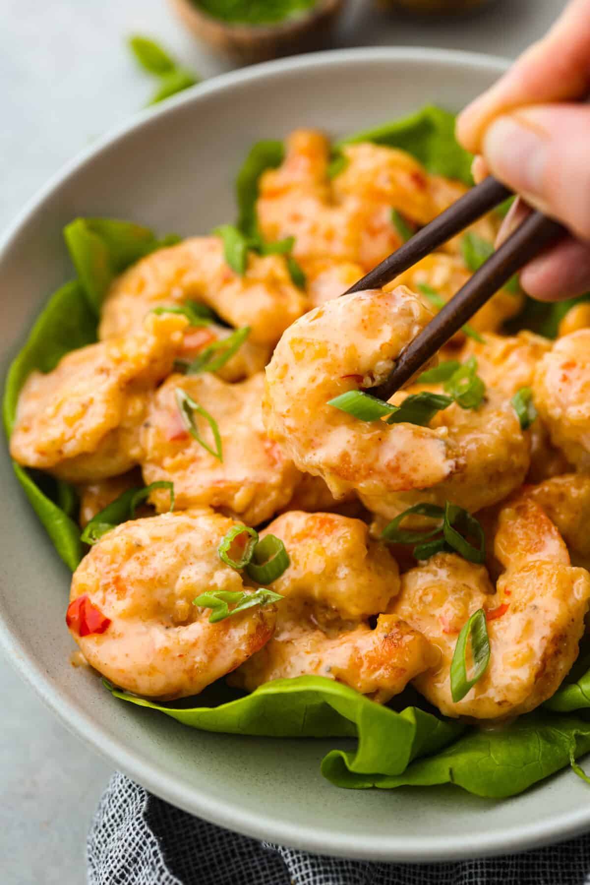This Copycat Bang Bang Shrimp is a replica of everyone's favorite shrimp appetizer! Sweet shrimp are fried until crispy, then tossed in a spicy, creamy mayo, and topped with chives. Perfect for sharing! Picking up a piece of shrimp with chopsticks