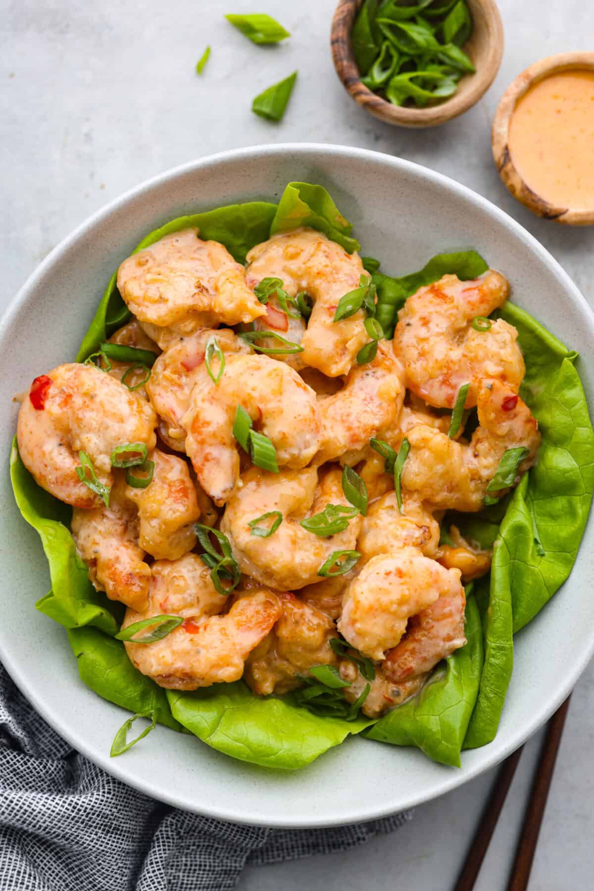 This Copycat Bang Bang Shrimp is a replica of everyone's favorite shrimp appetizer! Sweet shrimp are fried until crispy, then tossed in a spicy, creamy mayo, and topped with chives. Perfect for sharing! Bang bang shrimp served over a bed of greens in a white bowl.