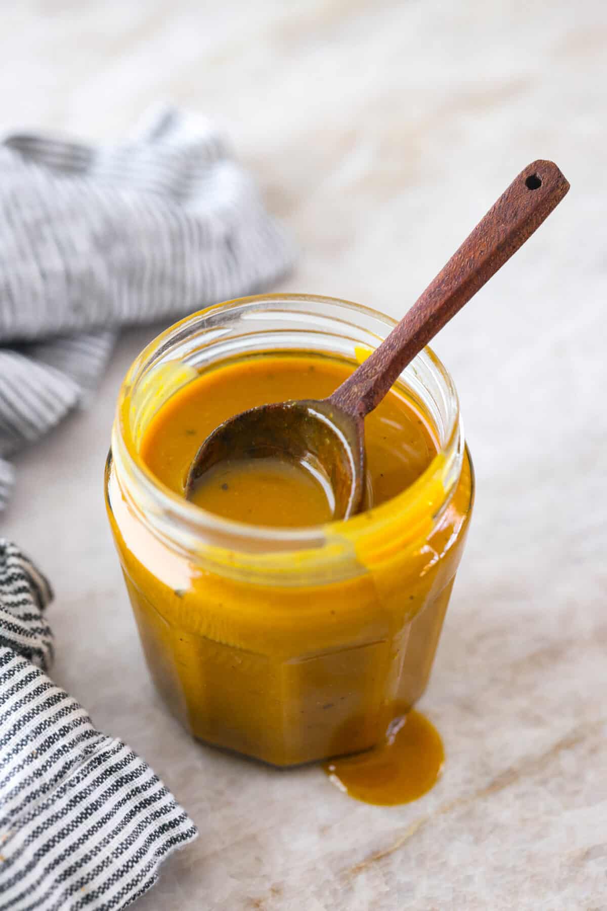 Smoky, tangy, and sweet, your taste buds will be begging you for more of this Mustard BBQ Sauce! It's the perfect addition to your summer cookouts this year, adding the best flavor to grilled meats! A glass jar filled with mustard bbq sauce. There is a wooden spoon in the jar as well.