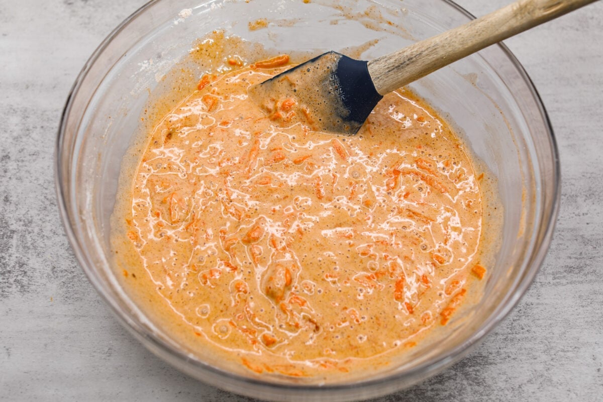 Stunning carrot cake roll is a wonderful joining of deliciously spiced carrot cake, swirled with tangy cream cheese frosting. It looks fancy but it's easy to make and so perfect for Easter and Spring themed celebrations! Carrot cake batter in a glass bowl.