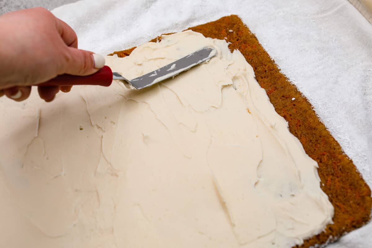 Stunning carrot cake roll is a wonderful joining of deliciously spiced carrot cake, swirled with tangy cream cheese frosting. It looks fancy but it's easy to make and so perfect for Easter and Spring themed celebrations! Spreading the cream cheese filling over the cake
