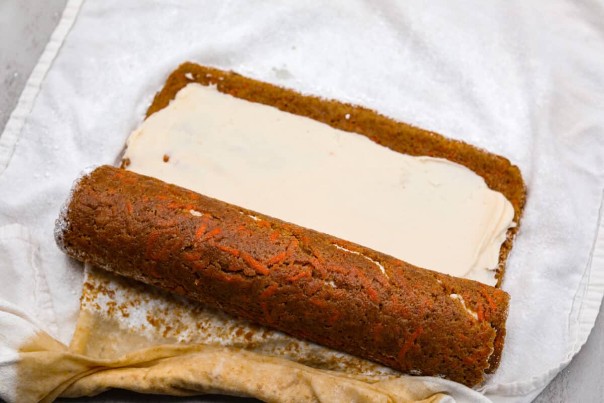 Stunning carrot cake roll is a wonderful joining of deliciously spiced carrot cake, swirled with tangy cream cheese frosting. It looks fancy but it's easy to make and so perfect for Easter and Spring themed celebrations! Rolling up the cream cheese filled carrot cake.