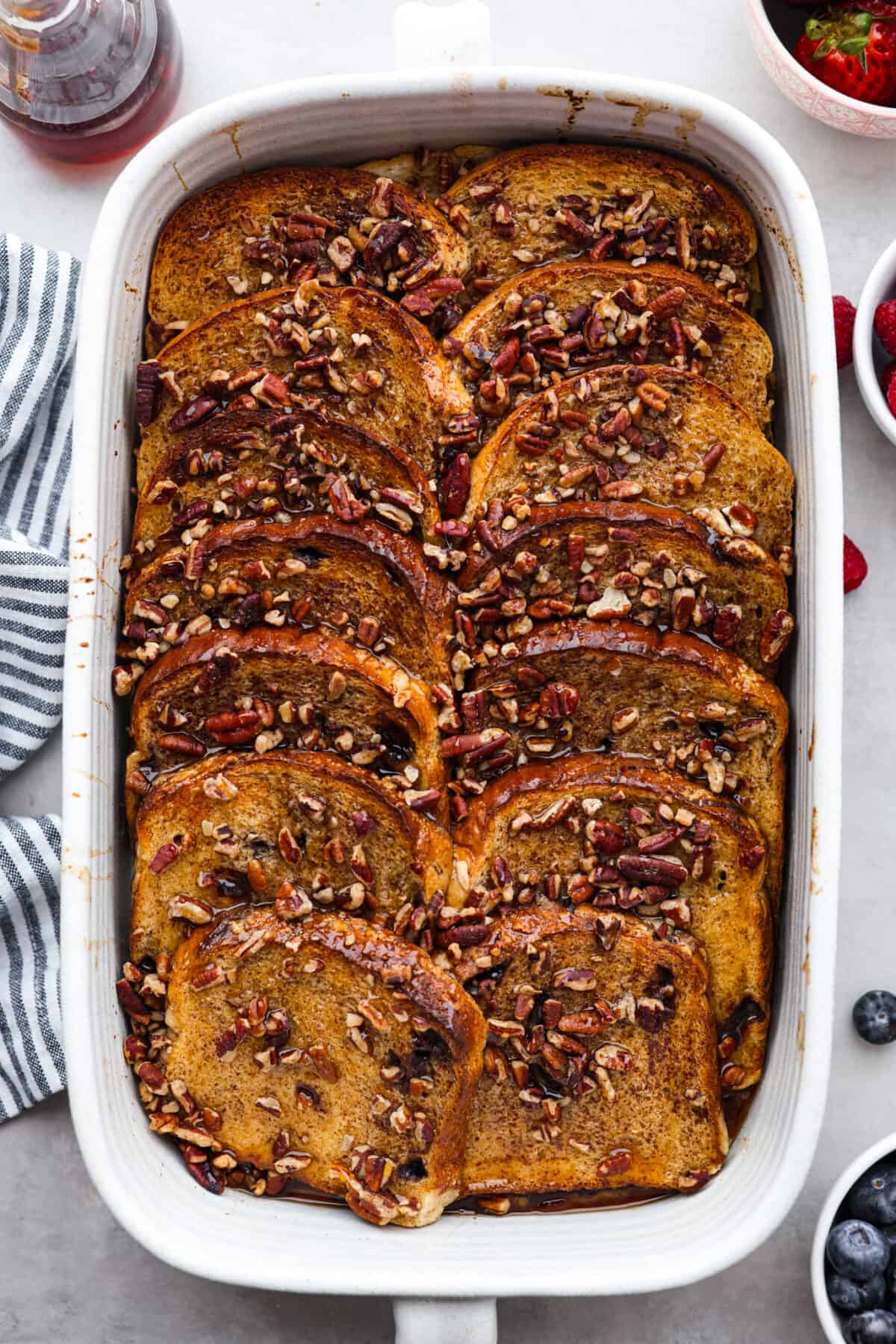 Cinnamon French toast bake is a warm and satisfying breakfast that's loaded with soft and sweet spiced bread all drizzled in maple syrup. Your family will go crazy over this insanely delicious (and easy-to-make) breakfast! Baked French toast in a baking dish, topped with pecans.