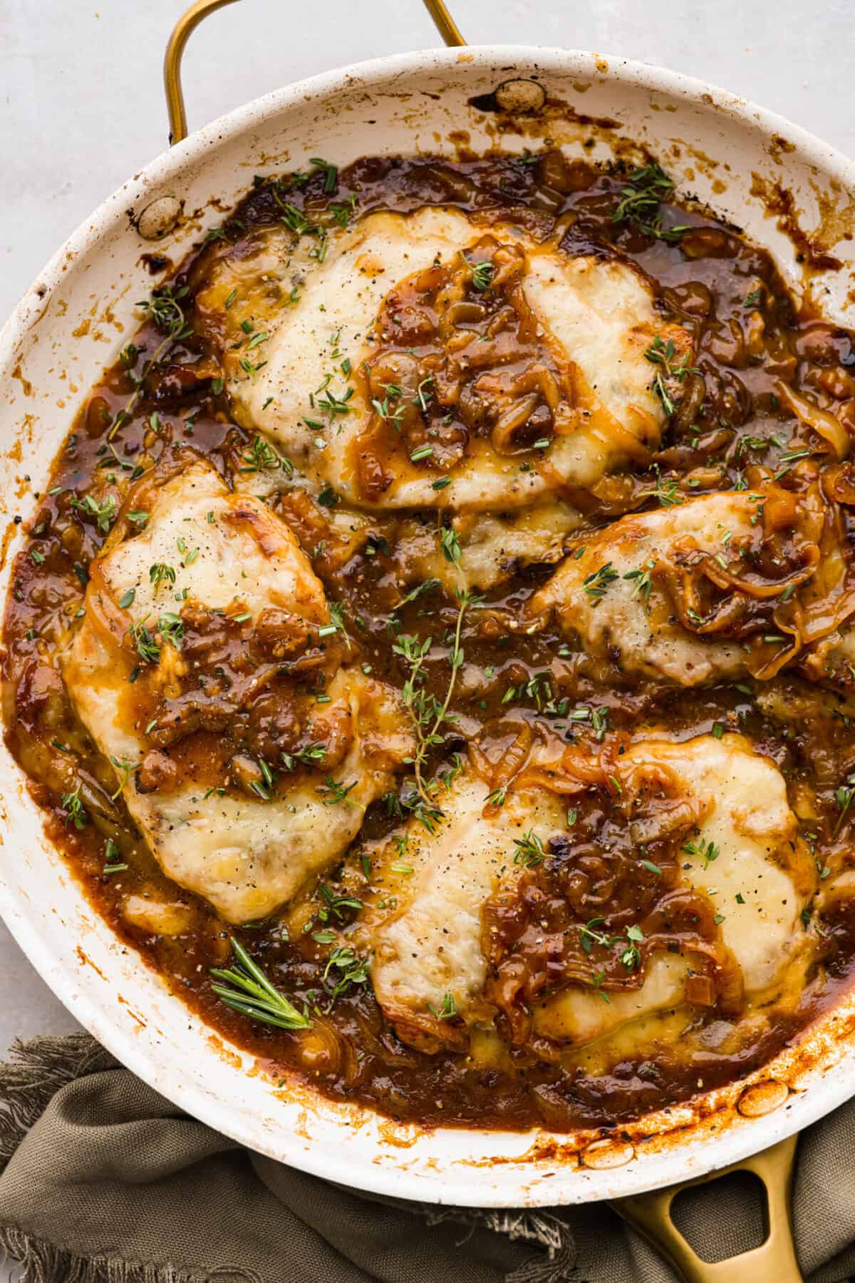 French Onion Pork Chops have all of the wonderful flavors of the classic soup in pork chop form! Caramelized onions and seared pork chops are joined with a savory sauce and two types of cheese for an amazing meal. Everything is cooked in one pan for a quick and easy weeknight dinner! 4 pork chops in a skillet topped with cheese and onion gravy.