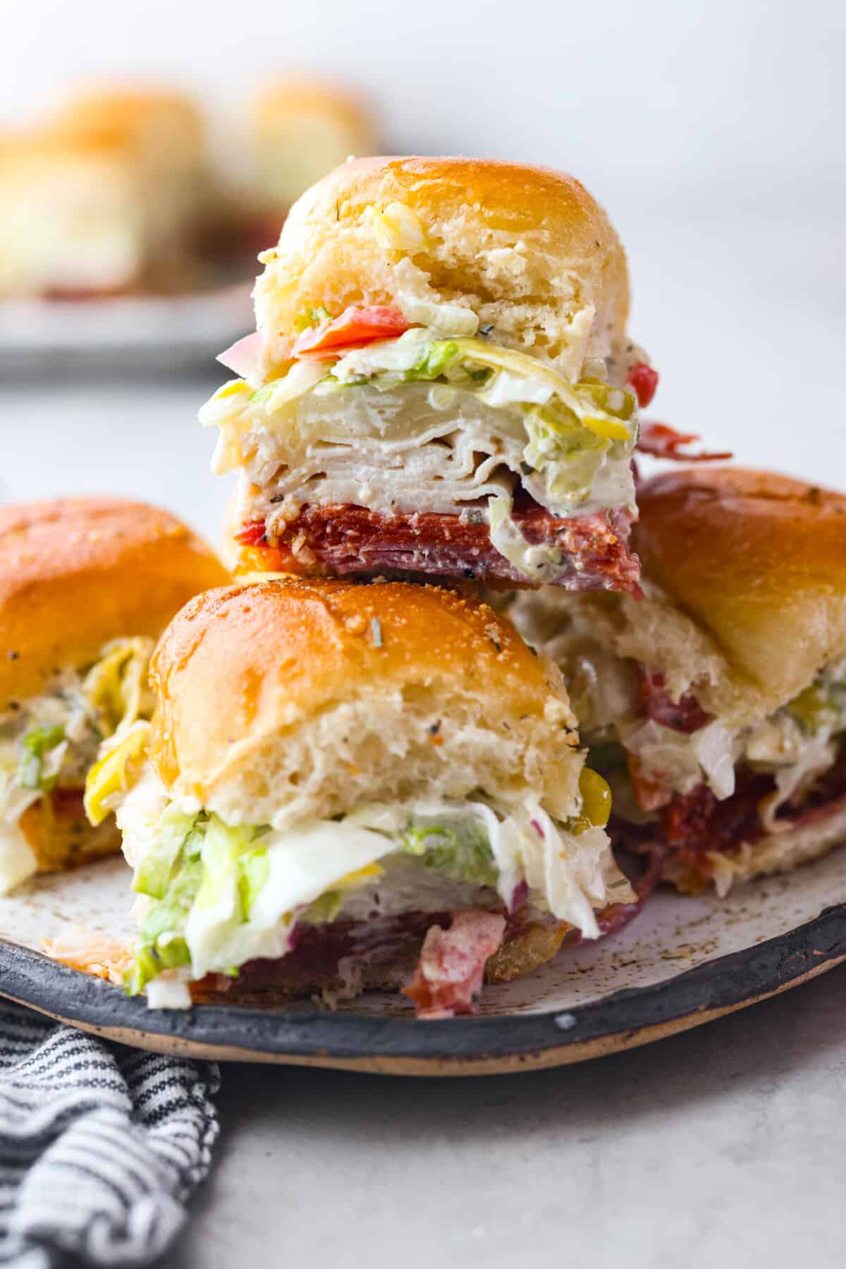 The classic grinder sandwich made into sliders to share! You've got Hawaiian rolls topped with layers of pepperoni, salami, turkey, provolone, and creamy grinder salad. And to top things off- each roll is brushed with a buttery parmesan glaze and baked to golden brown perfection. Grinder sliders stacked on top of each other.