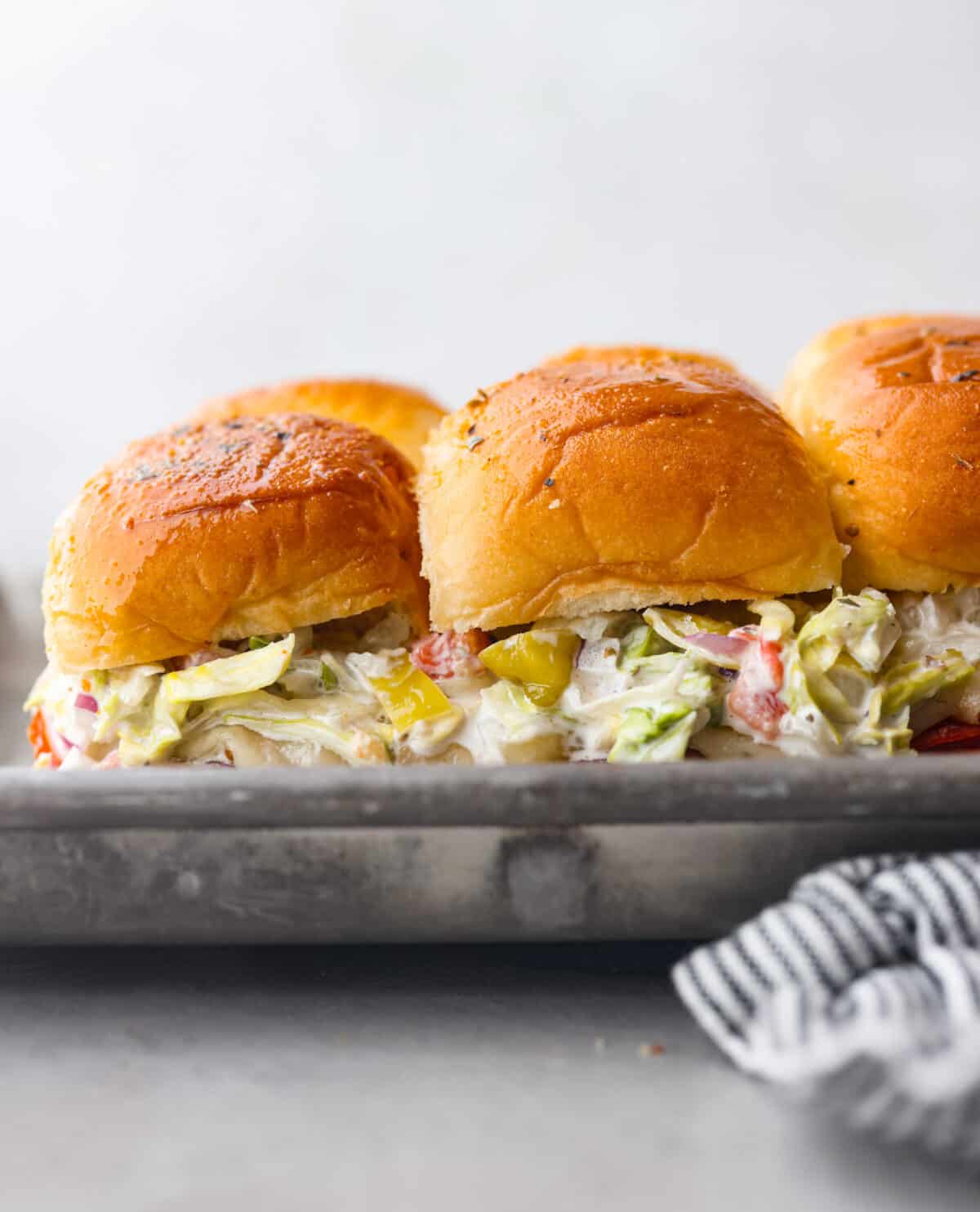 The classic grinder sandwich made into sliders to share! You've got Hawaiian rolls topped with layers of pepperoni, salami, turkey, provolone, and creamy grinder salad. And to top things off- each roll is brushed with a buttery parmesan glaze and baked to golden brown perfection. Grinder sliders in the pan.
