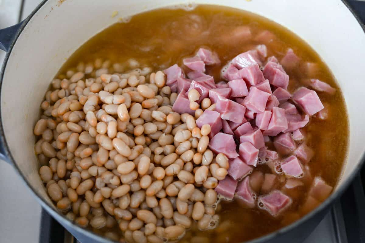 Comforting ham and bean soup is a classic and hearty soup. It's loaded with creamy white beans, smoky ham, and tender veggies. It's the perfect soup for using up your leftover ham and super easy to make on those busy weeknights. Third process photo of the beans and ham added to the pot.