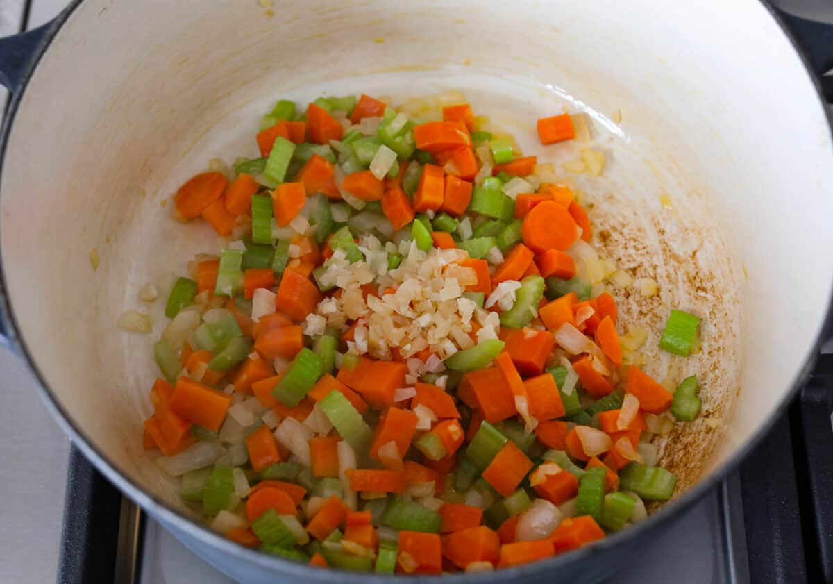 Comforting ham and bean soup is a classic and hearty soup. It's loaded with creamy white beans, smoky ham, and tender veggies. It's the perfect soup for using up your leftover ham and super easy to make on those busy weeknights. First process photo of the vegetables and garlic sautรฉing in a pot.