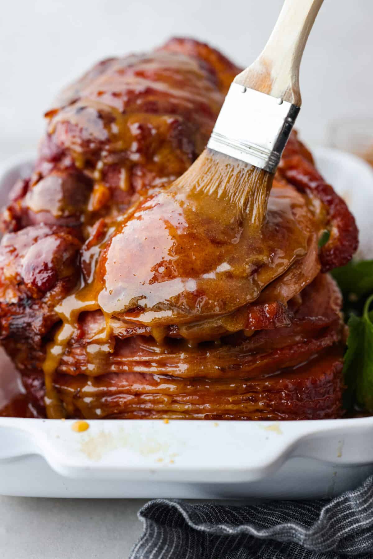 This honey-glazed ham is coated with delicious brown sugar and sweet honey glaze! It’s tender and juicy and goes with everything which makes it ideal for any holiday meal! Honey glazed ham being basted with extras of the honey brown sugar mixture.