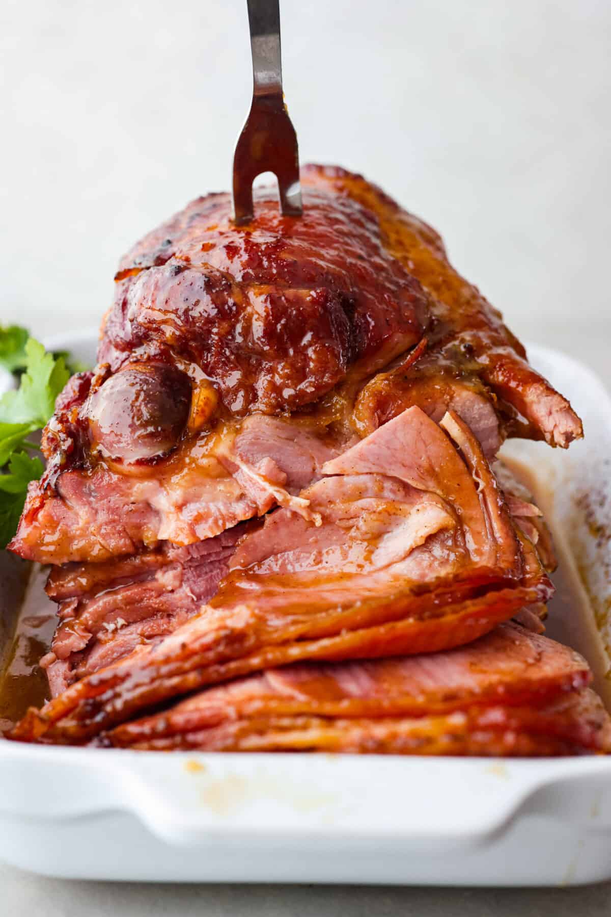 This honey-glazed ham is coated with delicious brown sugar and sweet honey glaze! It’s tender and juicy and goes with everything which makes it ideal for any holiday meal! Front view of the ham being cut into slices.