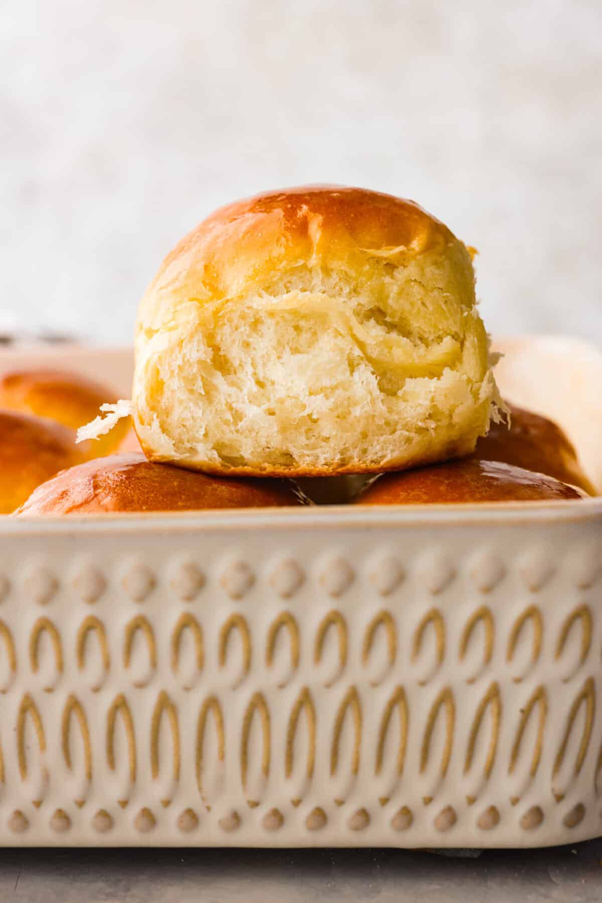 Perfectly soft buttery rolls will be your classic go-to roll recipe! They are tender fluffy, and baked with a buttery golden top. These rolls are sure to be a family favorite! Close view of a perfectly soft buttery roll stacked on top of the pan of fresh baked rolls.