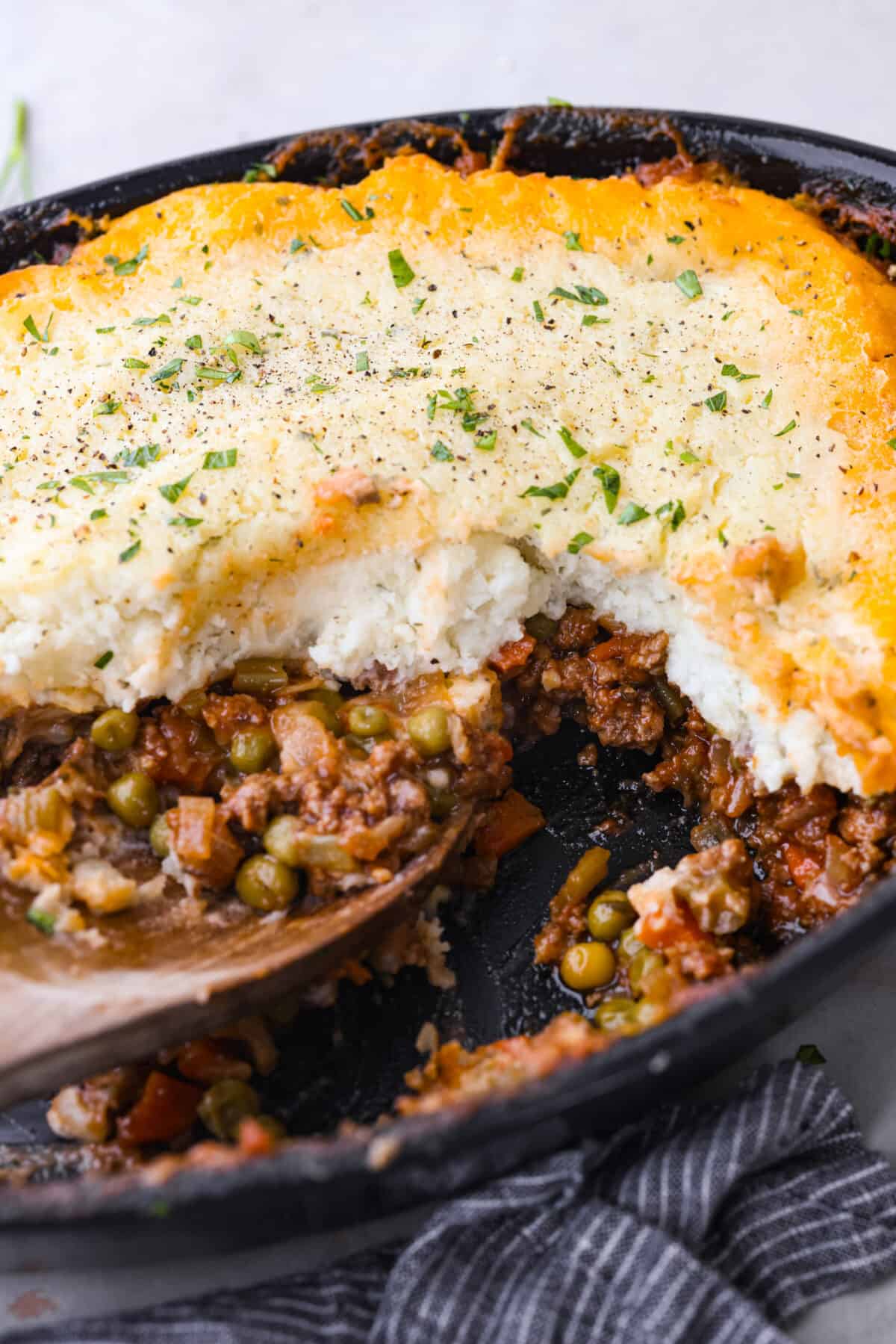 This easy Shepherd's Pie recipe is made with a saucy ground beef base, vegetables and creamy mashed potatoes. It's a hearty make-ahead meal for busy weeknights or Sunday dinner! Closeup of Shepherd's pie with a serving taken out of it.
