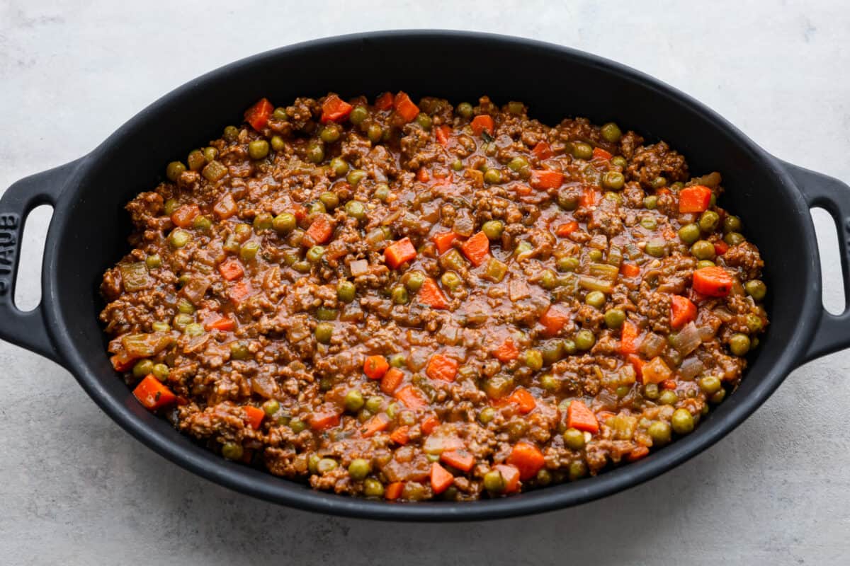 Preheat the oven to 375 degrees Fahrenheit. In a large, deep skillet, heat the oil over medium-high heat and cook the carrots, celery, and onion until softened, about 5 minutes. Add the beef and cook until thoroughly browned and no pink remains. Break it up into pieces as it cooks. Add the minced garlic and cook for 1 additional minute. Whisk together beef broth and cornstarch. Add it to the skillet, along with the tomato paste, Worcestershire sauce, herbs, and salt and pepper. Stir in the frozen peas and cook for 5 minutes, until the sauce has thickened. Mashed Potatoes Add the peeled and diced potatoes to a large pot and fill with cold water until the potatoes are covered. Add 2-3 large pinches of kosher salt. Place the pot over high heat and bring to a boil. Reduce heat to maintain a rolling boil and cook until tender, about 12-15 minutes. Drain the potatoes into a colander. Return the potatoes to the pot and either run them through a potato ricer or use a hand masher to mash them well. Add the butter, warm half and half, and Boursin cheese to the potatoes and mash until creamy. Taste and season with salt and pepper if needed. Spread the potatoes evenly over the top of the meat mixture. Bake the Shepherd's pie uncovered for 25-30 minutes until the edges are bubbling. Sprinkle with fresh chopped parsley and serve. Adding the Shepherd’s pie filling to a baking dish.