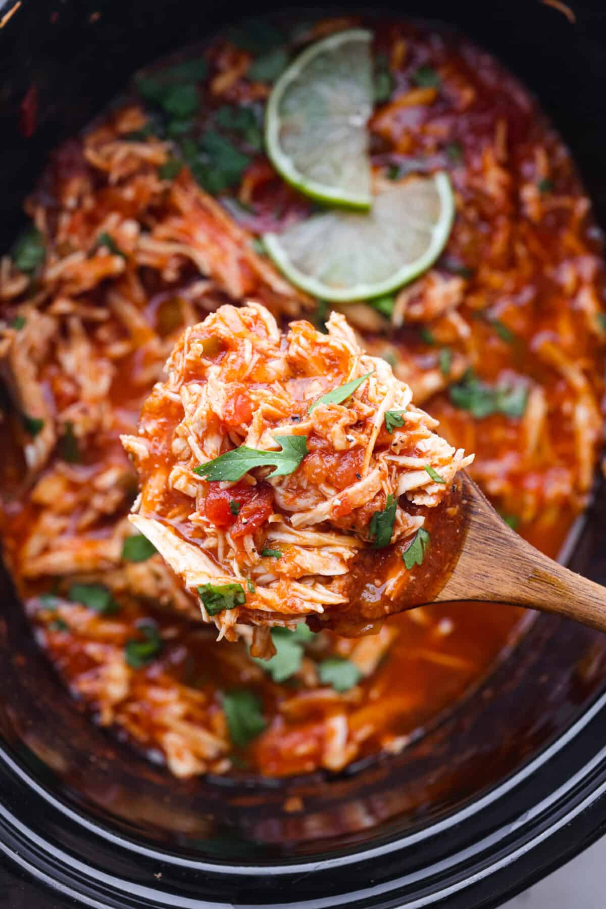 Weeknight dinner made easy with this crockpot salsa chicken! Tender flavorful chicken that only takes 5 ingredients to make. It's a versatile recipe the whole family will love! Close view of a serving spoon lifting chicken from the slow cooker.