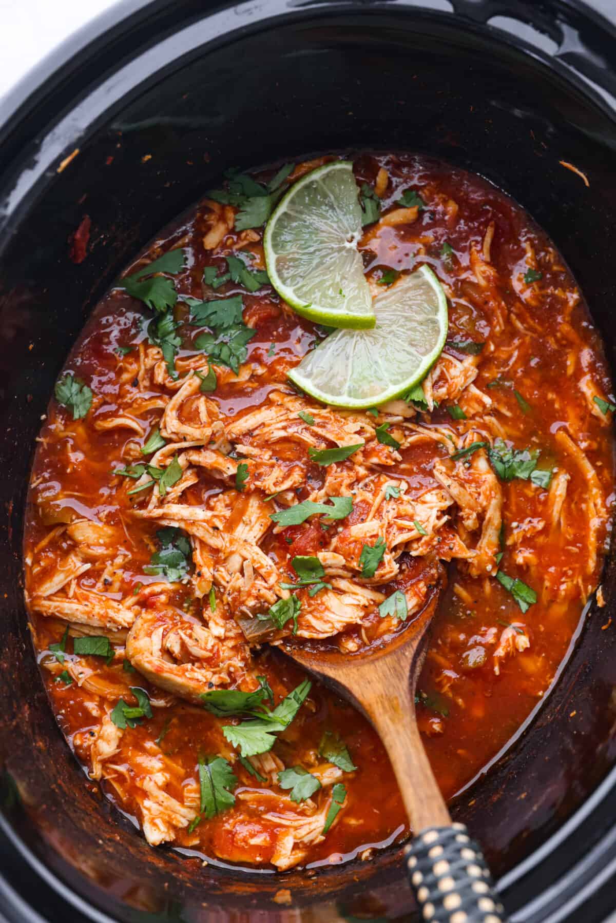 Weeknight dinner made easy with this crockpot salsa chicken! Tender flavorful chicken that only takes 5 ingredients to make. It's a versatile recipe the whole family will love! Top view of salsa chicken in the crockpot with a serving spoon.
