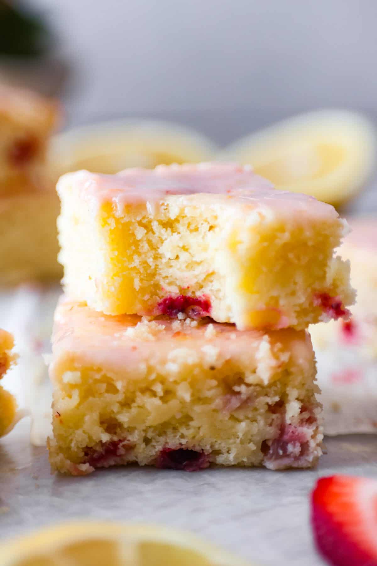 Tender and moist, strawberry lemon blondies are loaded with plenty of sweet, juicy strawberries that are joined with just enough tangy lemon flavor. These amazing bars are buttery, thick and the perfect spring and summer dessert! Closeup of 2 strawberry lemon blondies stacked on top of each other.