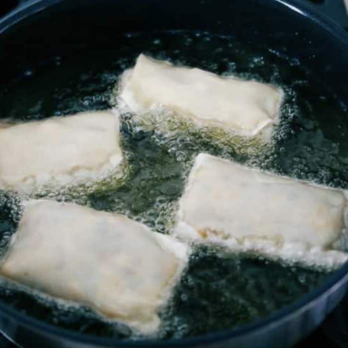 These are the BEST Southwest chicken egg rolls! It's aย colorfulย combination of corn, black beans, fresh veggies, shredded cheese, and chicken. This tasty mixture is flavored in savory southwestย seasonings then fried in a crispy egg roll wrapper. These won't last long at your next party! Fifth photo of the egg rolls placed in the hot oil to fry.
