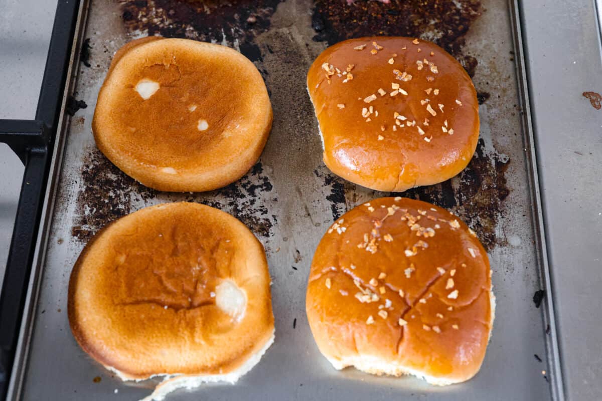 Create the most flavorful, juicy Mushroom Swiss Burger! Perfectly seasoned ground beef is topped with sautรฉed buttery mushrooms and melty Swiss cheese then loaded on fluffy buns for a gourmet burger that's easy to make at home! A phot showing how to add butter and sesame seeds to the buns.