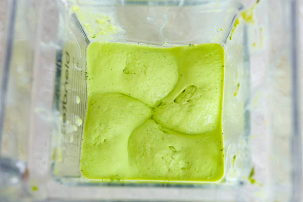 This dressing is packed with flavor and so creamy! It's delicious on salads, burrito bowls, tacos, and even burgers and wraps. I love how quick and easy it is to make with simple ingredients, and it has the perfect balance of tangy, nutty and subtly sweet flavors. Overhead view of blender with ingredients for avocado dressing all blended together.
