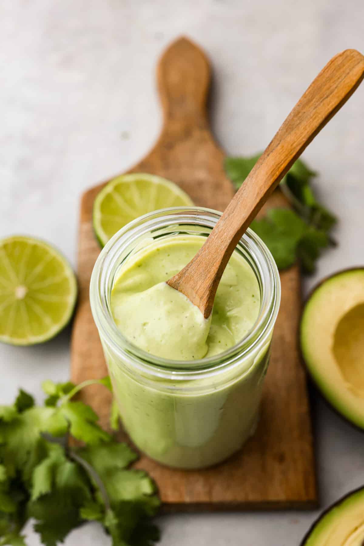 This dressing is packed with flavor and so creamy! It's delicious on salads, burrito bowls, tacos, and even burgers and wraps. I love how quick and easy it is to make with simple ingredients, and it has the perfect balance of tangy, nutty and subtly sweet flavors. Overhead view of avocado dressing in glass jar with wood spoon sticking out.