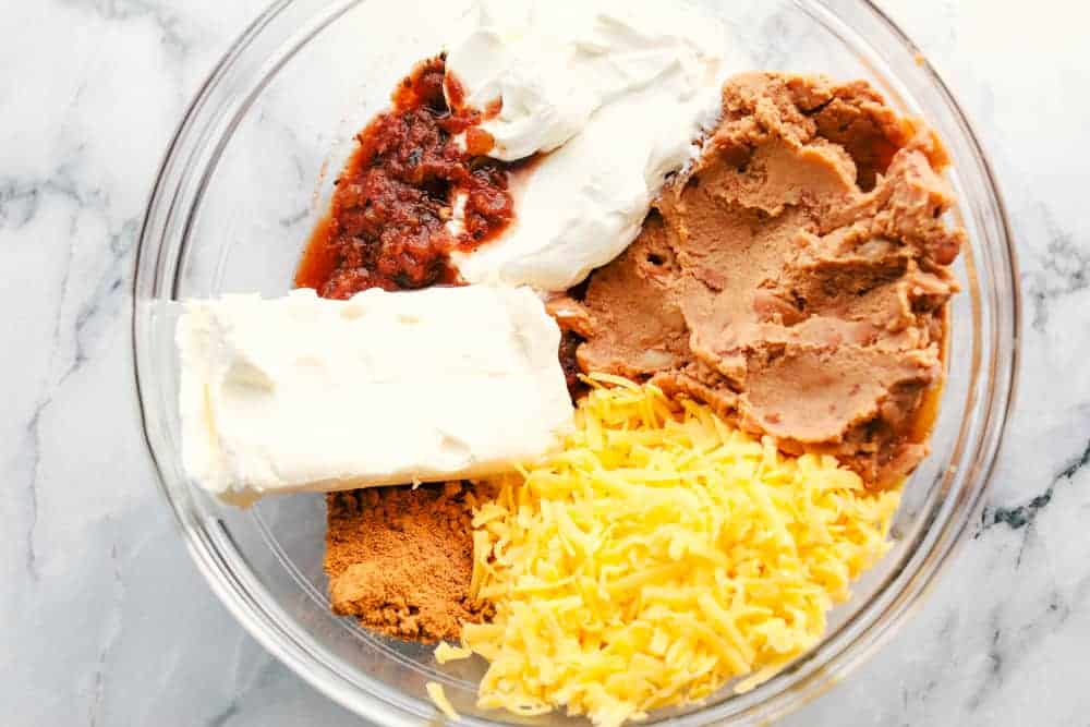 Bring out the chips and start dipping because this is the most addicting bean dip you will ever have! It's creamy, cheesy, and loaded with tasty Mexican-inspired flavors. Garnish with toppings, and take this to your next gathering! Process shot of ingredients added to a large bowl.