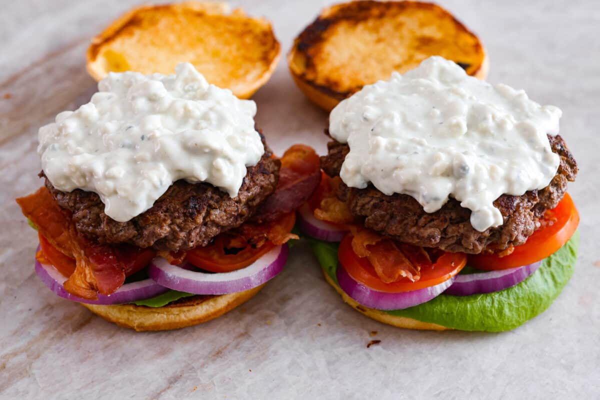 Get ready to be blown away by this Blue Cheese Burger! It's thick, juicy, and filled with flavor. If you love blue cheese dressing, this recipe is for you! That unique tangy flavor is the perfect addition to the juiciest patty ever. Side view of blue cheese burgers with all of the toppings without the top bun.