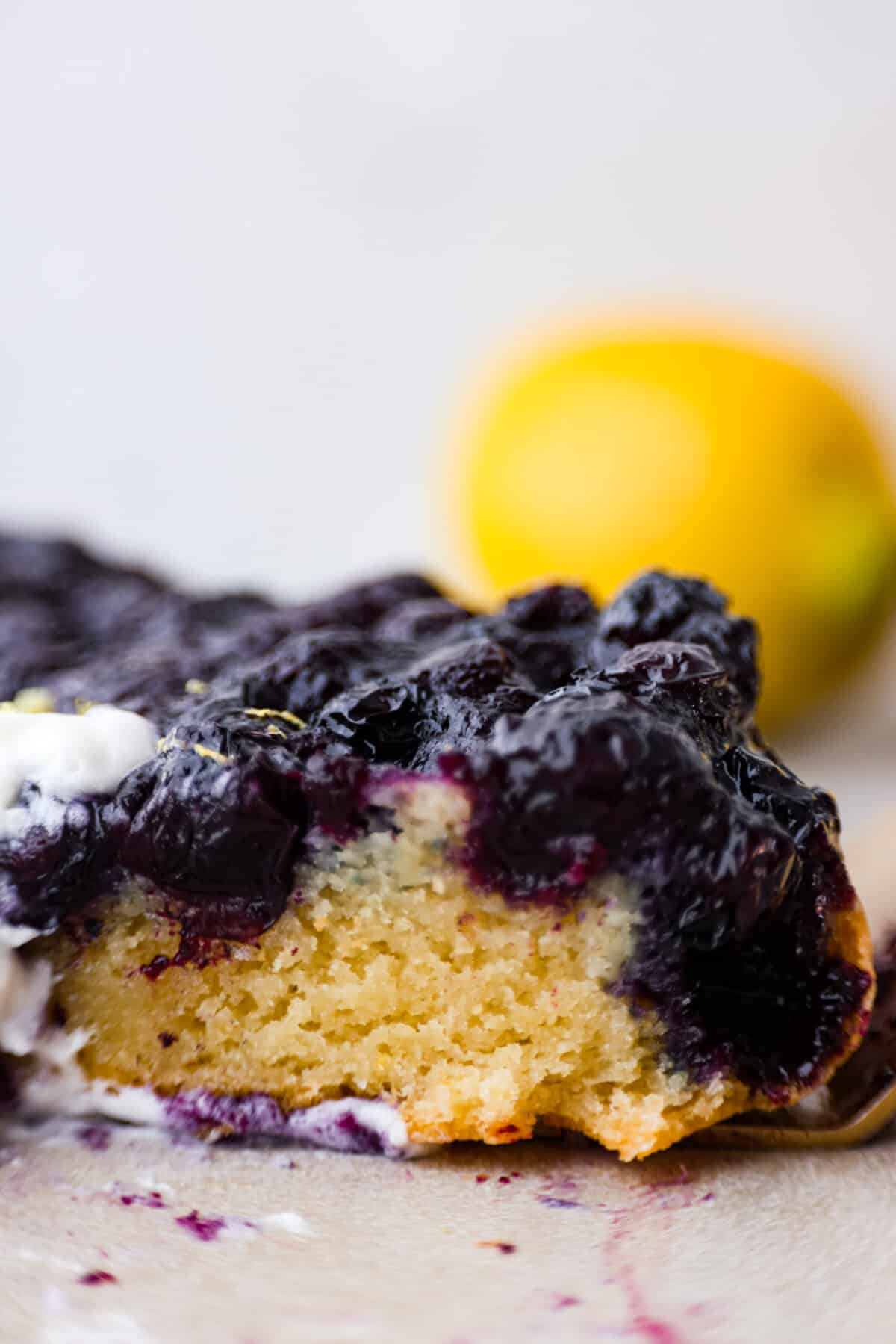 Be prepared to fall in love with this blueberry lemon upside-down cake! A delicious and moist lemon sponge cake bursting with juicy caramelized blueberries on top! Close view of a slice of blueberry lemon upside-down cake.