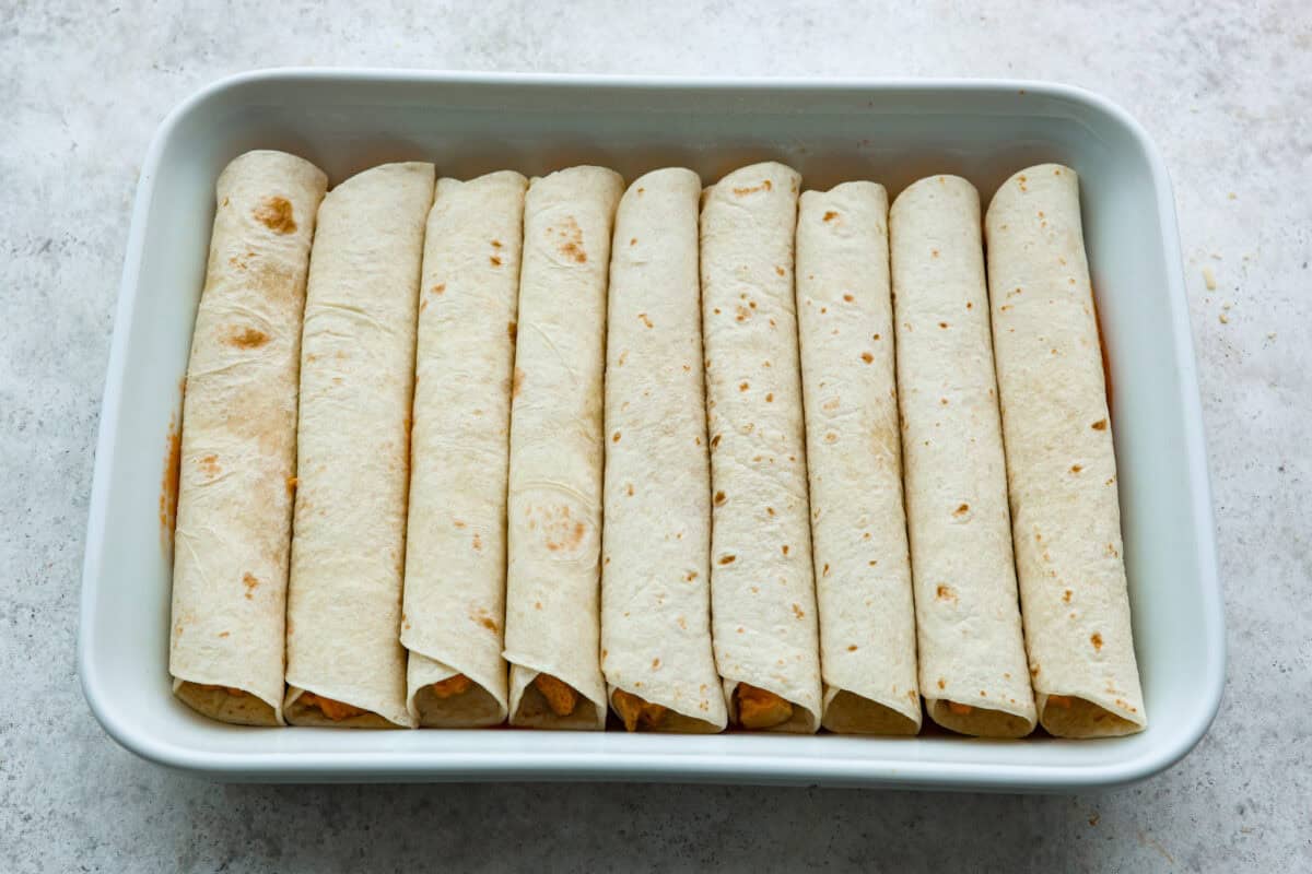 A new enchilada is in town! Get ready for the bold flavors in these buffalo chicken enchiladas! Chicken enchiladas loaded with cheese and smothered in a creamy buffalo enchilada sauce. Sixth photo of the enchiladas layered in the baking dish.