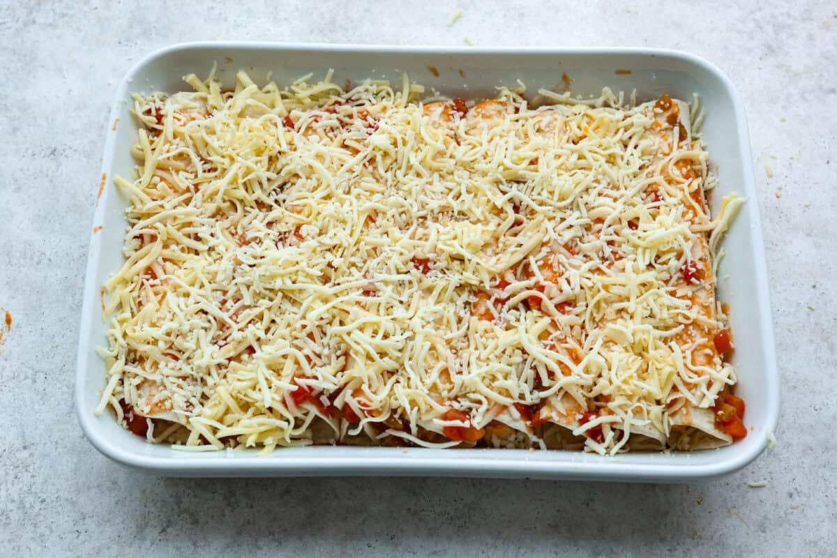 A new enchilada is in town! Get ready for the bold flavors in these buffalo chicken enchiladas! Chicken enchiladas loaded with cheese and smothered in a creamy buffalo enchilada sauce. Eighth photo of the cheese sprinkled on top of the buffalo chicken enchiladas before baking.