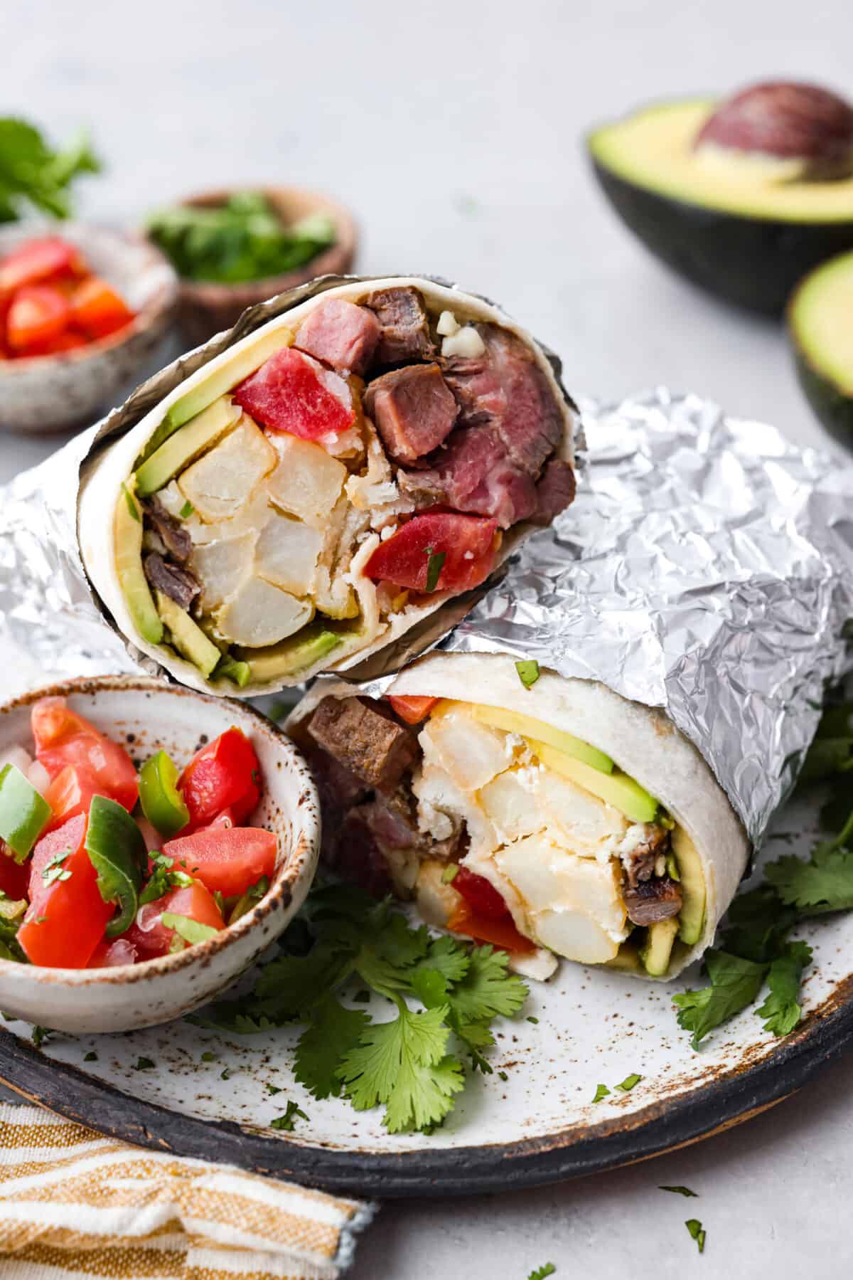 This delicious California Burrito is filled with well-seasoned grilled steak, pepper jack cheese, French fries, pico de Gallo, sour cream and avocado, all wrapped up in a warm flour tortilla. A flavorful lunch or dinner option that will be an absolute hit! A california burrito wrapped in tinfoil and sliced in half.