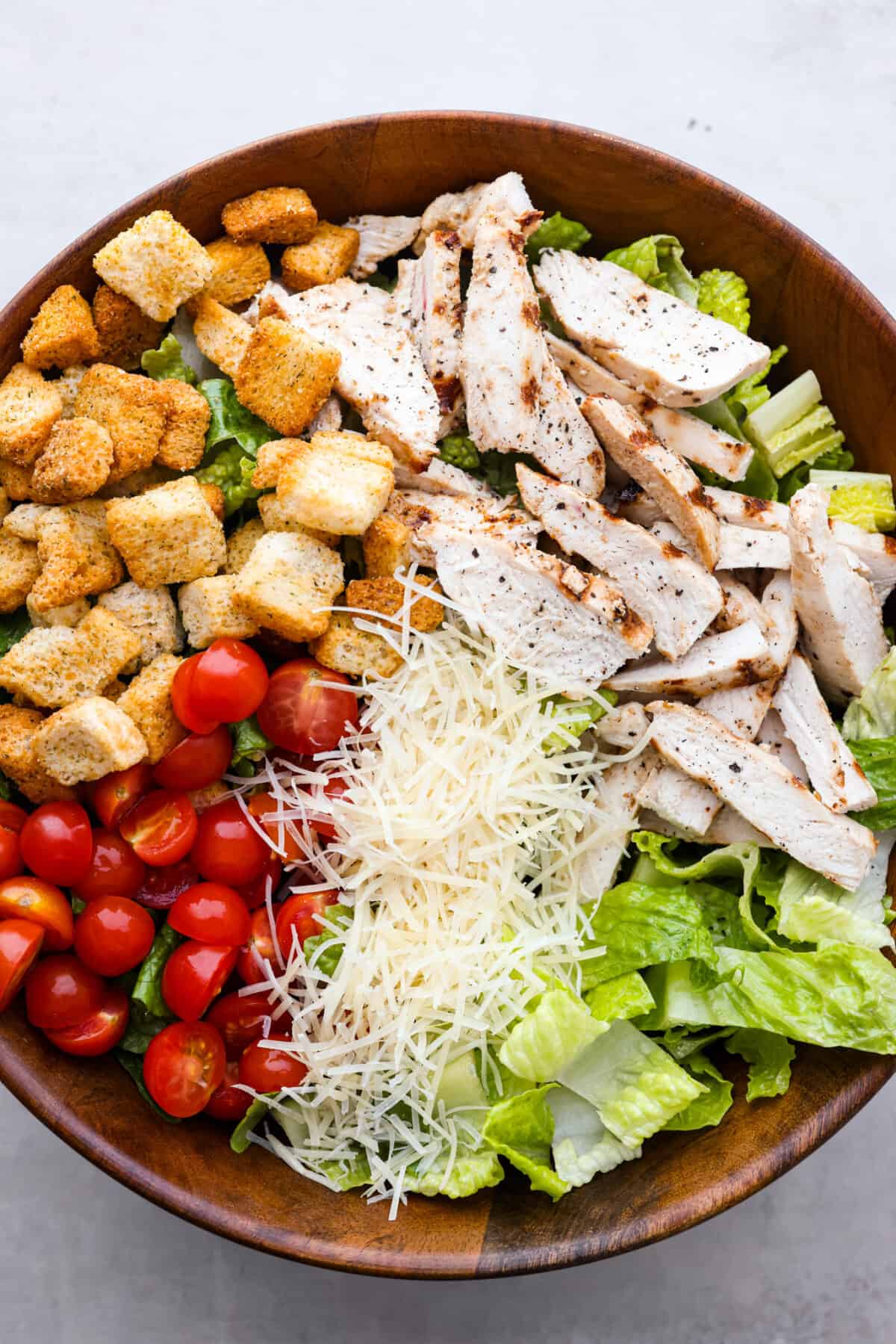 Fresh and delicious Grilled Chicken Caesar Salad is a crowd-pleasing hearty salad with tender grilled chicken, crisp romaine lettuce, cherry tomatoes, shredded parmesan cheese, and crunchy croutons! Grilled chicken caesar salad in a bowl. ready to be mixed.