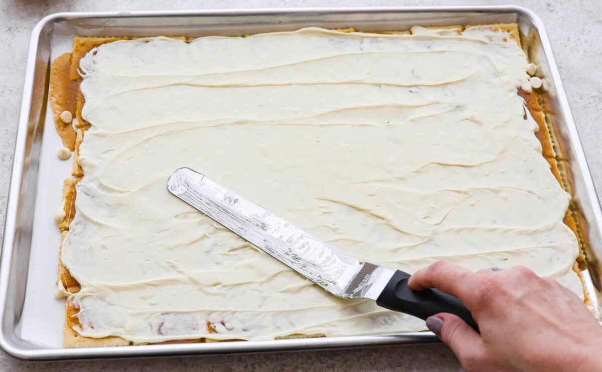Melted white chocolate being spread over saltine crackers to make churro crack. 
