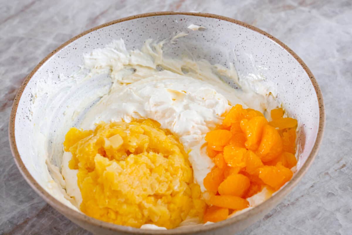 Serve this fun and delicious cookie salad as a dessert or side dish! Everyone will love the sweet fluffy pudding base mixed with mandarin oranges, crushed pineapple, and fudge stripes cookies. Third process photo of pineapple and mandarin oranges added to the pudding mixture.