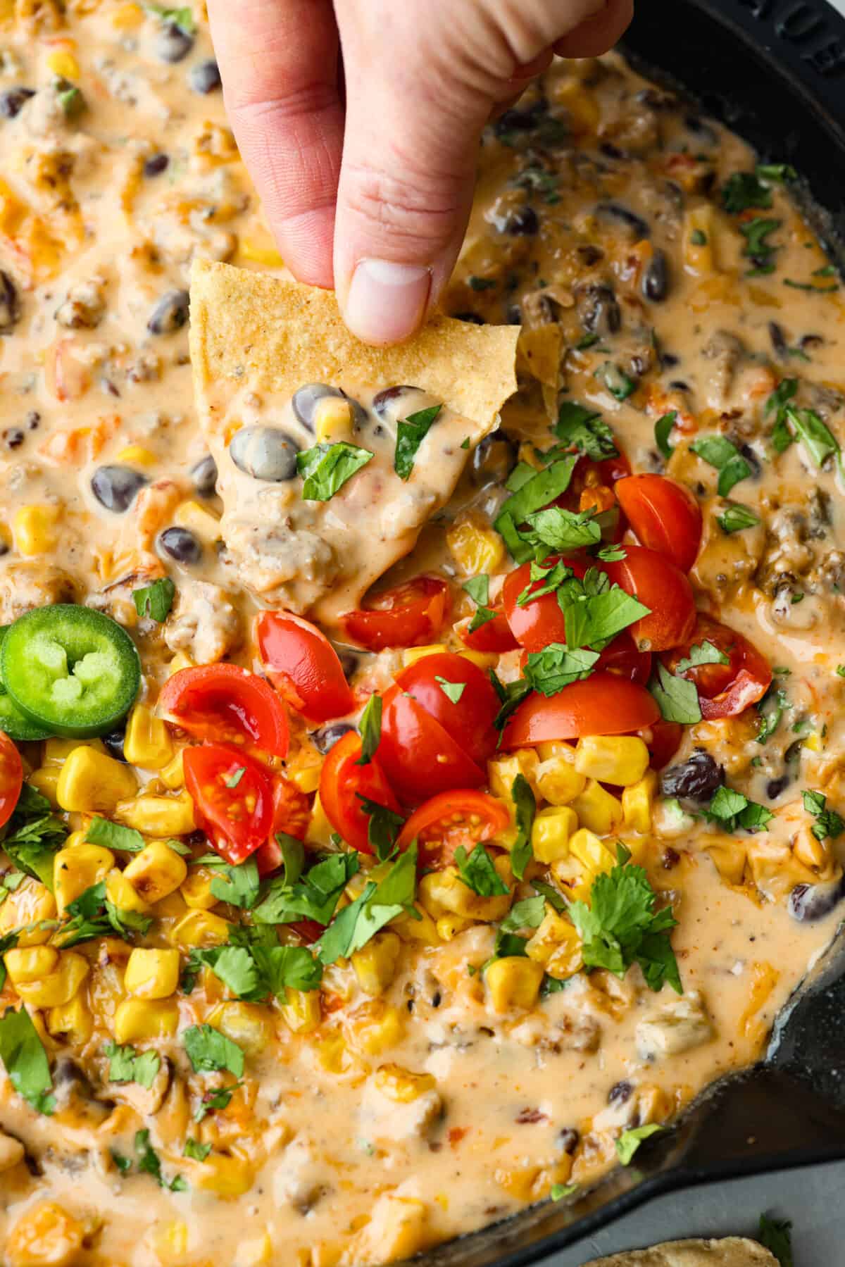 Get ready to rustle up some serious flavor with this Cowboy Queso! Packed with zesty sausage, hearty beans, and a kick of beer, it's the perfect dip for any gathering—just grab your tortilla chips and dig in! A chip being dipped in cowboy queso.