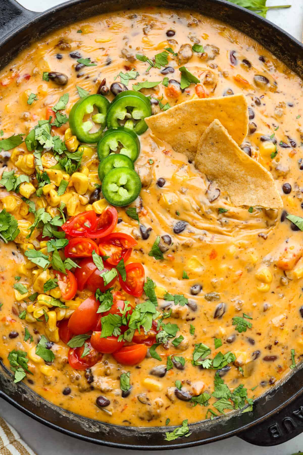 Get ready to rustle up some serious flavor with this Cowboy Queso! Packed with zesty sausage, hearty beans, and a kick of beer, it's the perfect dip for any gathering—just grab your tortilla chips and dig in! Close up of cowboy quest in a skillet with 2 tortilla chips dipped in it.