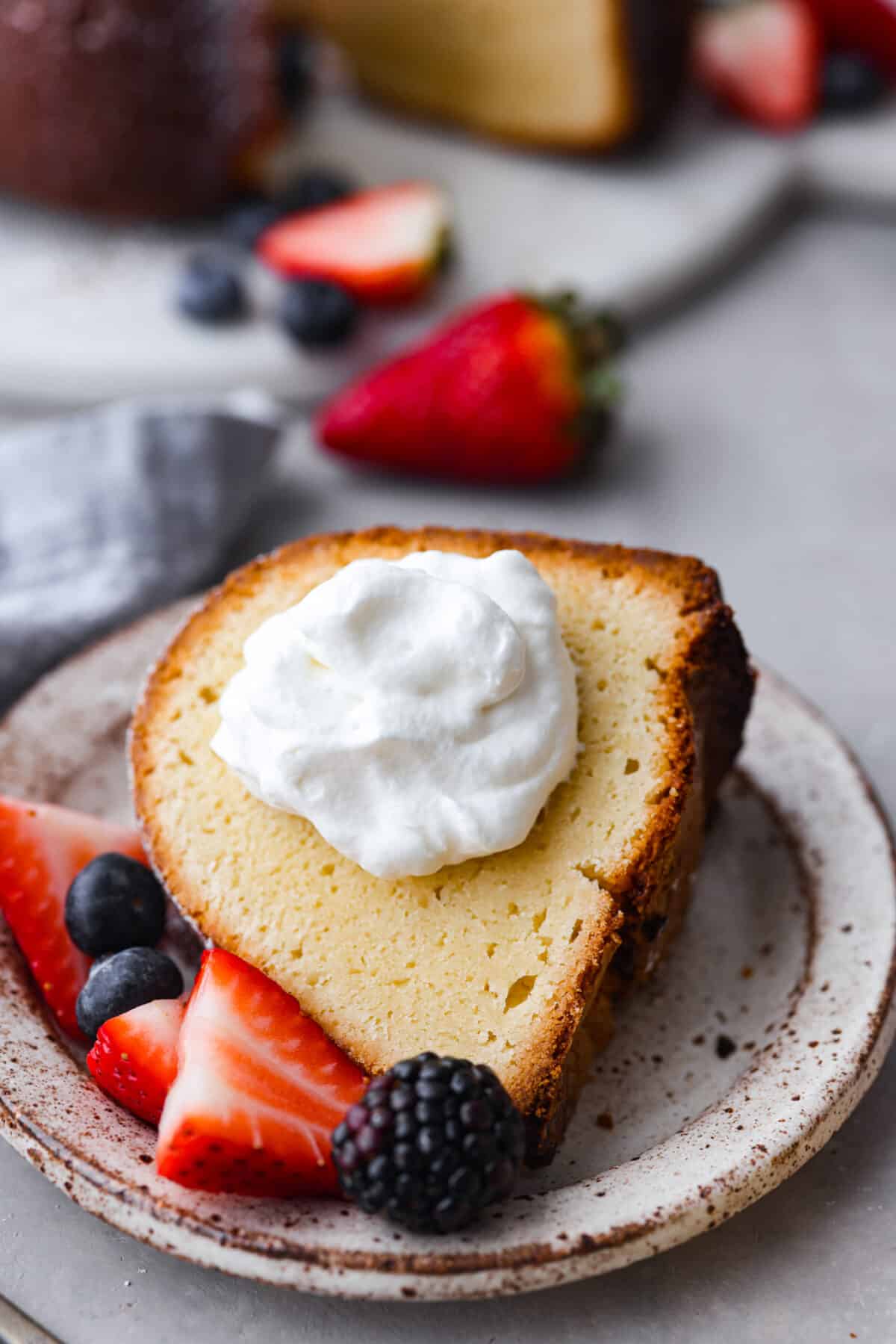 This Cream Cheese Pound Cake is a tender, moist, and flavorful dessert that's a new spin on traditional pound cake. Plus, it’s super simple to make! Top it off with whipped cream and fresh berries or enjoy plain! A slice of cake with a dollop of whipped cream on it.