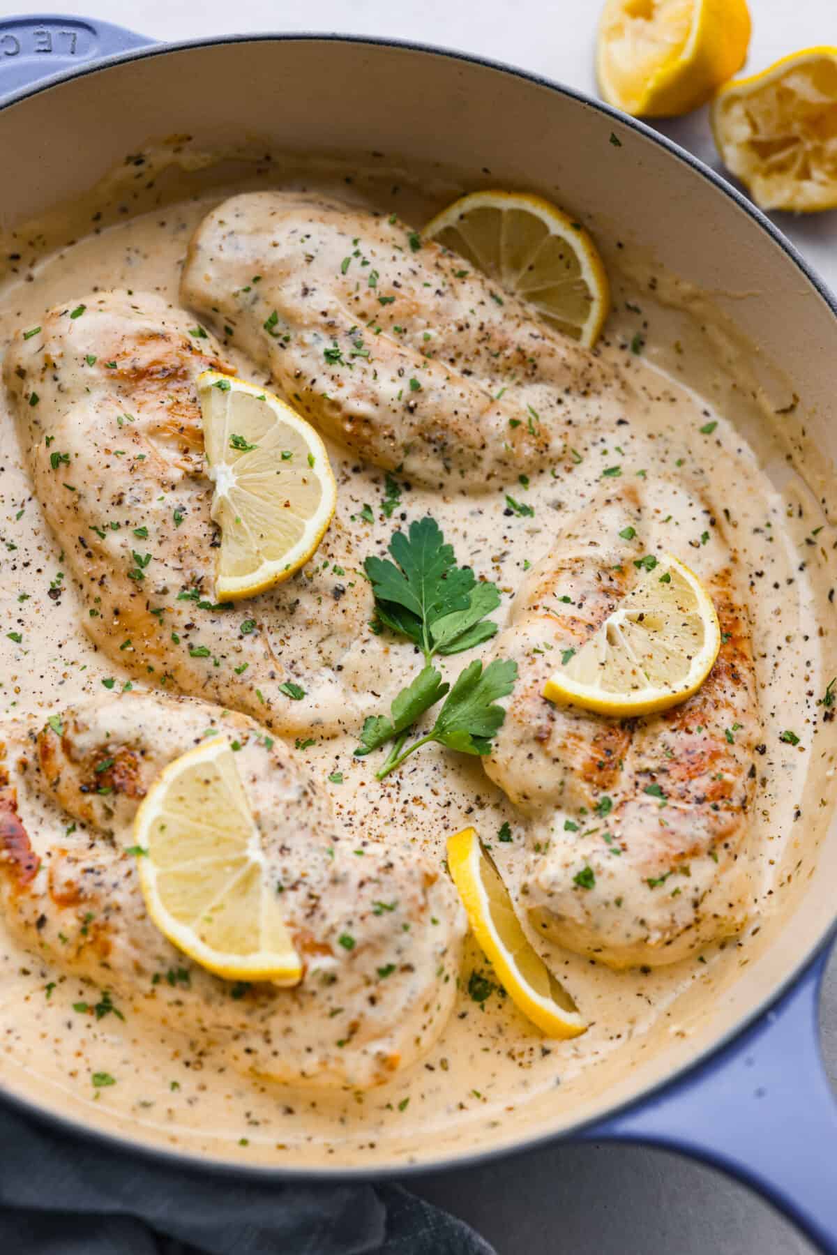 Creamy Lemon Parmesan Chicken is an incredible restaurant-quality meal you can make in under 30 minutes. Tender, juicy chicken is smothered in a creamy lemon parmesan sauce- itโs a meal the family will go crazy for!ย The finished creamy lemon parmesan chicken in a blue and white skillet, garnished with lemon slices and parsley.