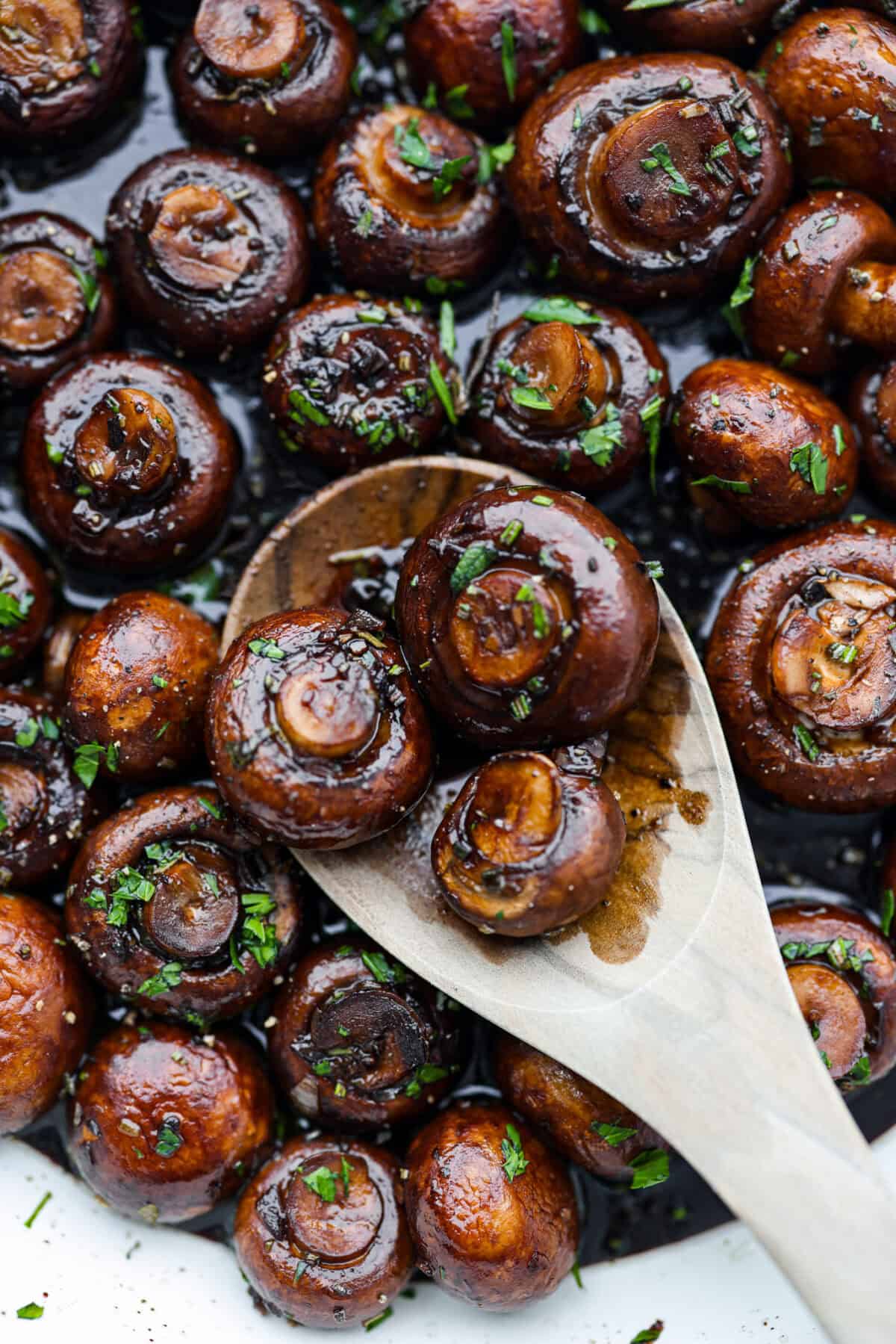 The depth of flavors in these garlic balsamic mushrooms is next level! Sauteed mushrooms are coated in a sweet balsamic sauce loaded with herbs. It's a simple and impressive side dish that only takes minutes to prepare. Close view of garlic balsamic mushrooms with a wood serving spoon.