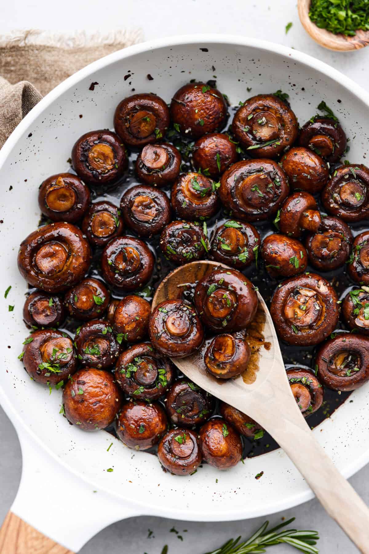The depth of flavors in these garlic balsamic mushrooms is next level! Sauteed mushrooms are coated in a sweet balsamic sauce loaded with herbs. It's a simple and impressive side dish that only takes minutes to prepare. Top view of garlic balsamic mushrooms in a skillet with a wood serving spoon.