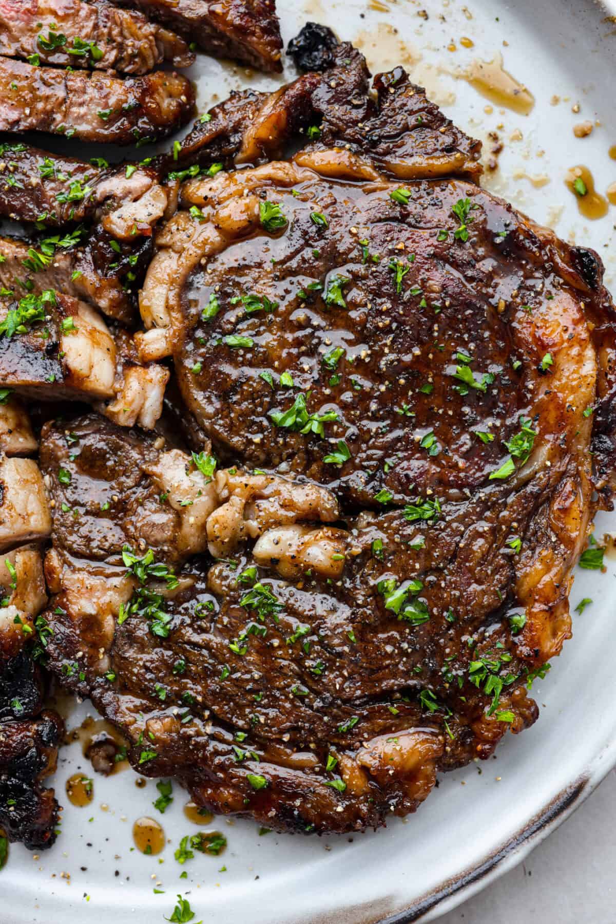 Fire up the grill for these mouthwatering Grilled Bourbon Steaks! Marinated in a blend of whiskey, brown sugar, and savory spices, these steaks are sure to be a hit at your next barbecue. A close up of grilled bourbon steak on a plate.