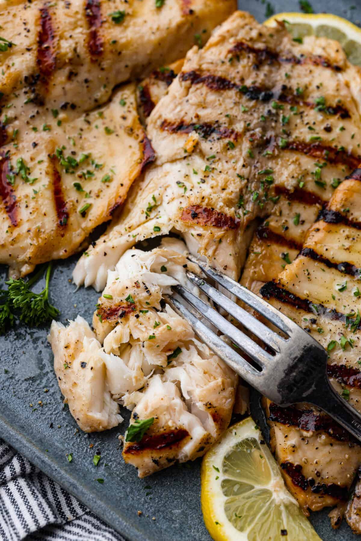 Fire up the grill! This grilled tilapia is deliciously seasoned and has the best flaky texture. Close of of tilapia on a plate with a fork.