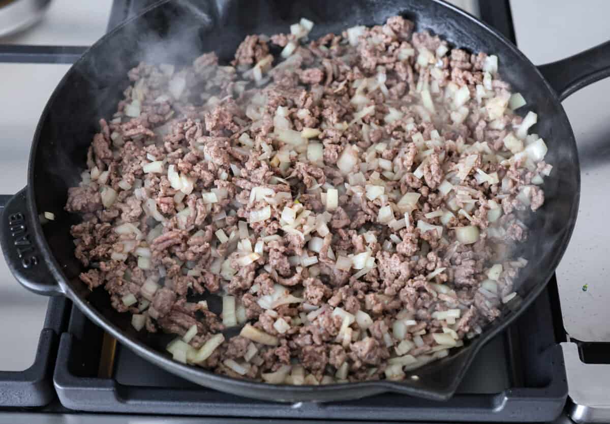 Get ready to enjoy a delicious and easy ground beef and broccoli stir-fry thatโs perfect for a quick weeknight dinner. This flavorful dish combines tender broccoli, savory beef, and a rich, tangy sauce, all served over steamed rice for a satisfying meal the whole family will love. Overhead shot of ground beef with onions cooking in a skillet.