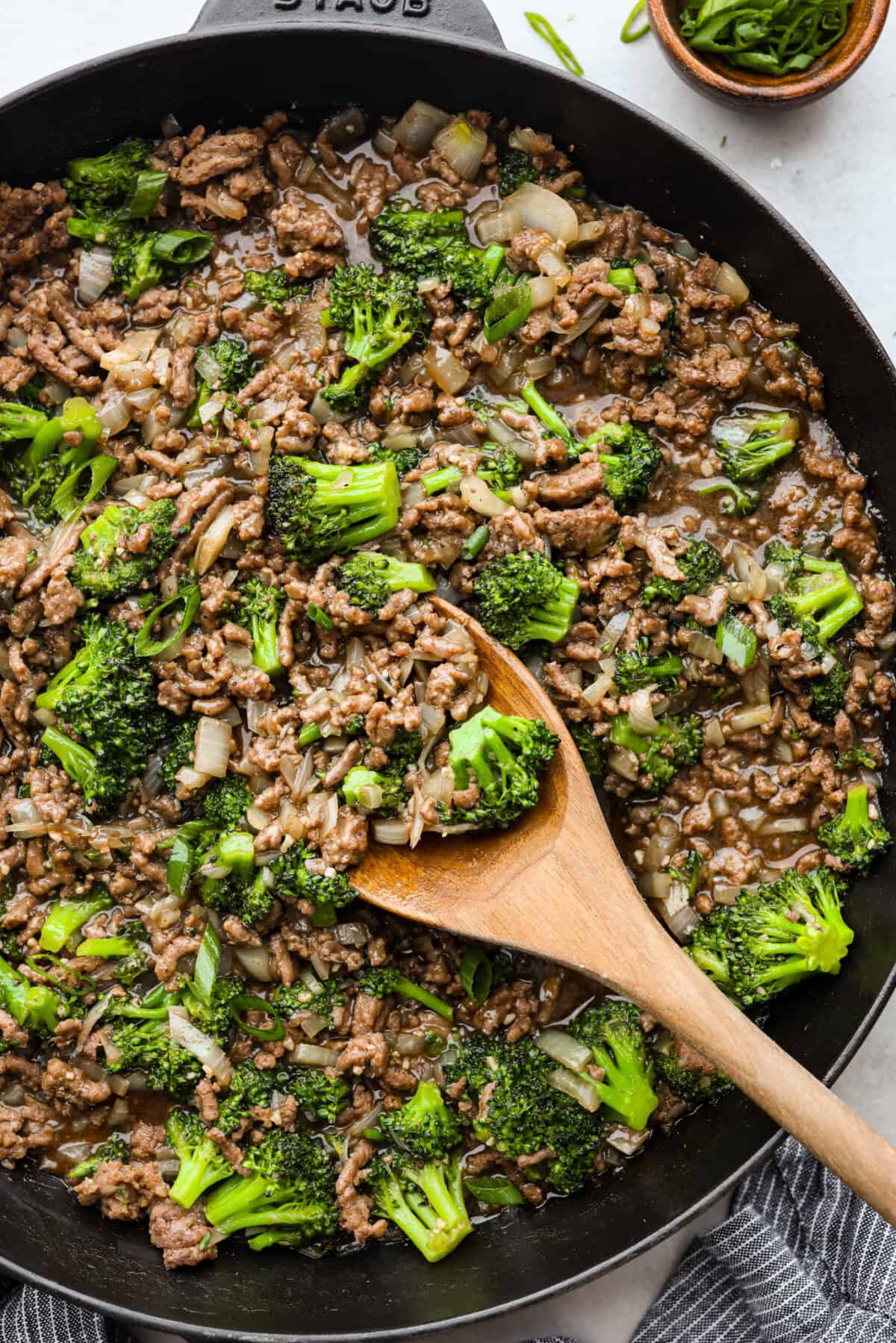 Get ready to enjoy a delicious and easy ground beef and broccoli stir-fry thatโs perfect for a quick weeknight dinner. This flavorful dish combines tender broccoli, savory beef, and a rich, tangy sauce, all served over steamed rice for a satisfying meal the whole family will love. Overhead shot of ground beef and broccoli in skillet with wooden spoon.