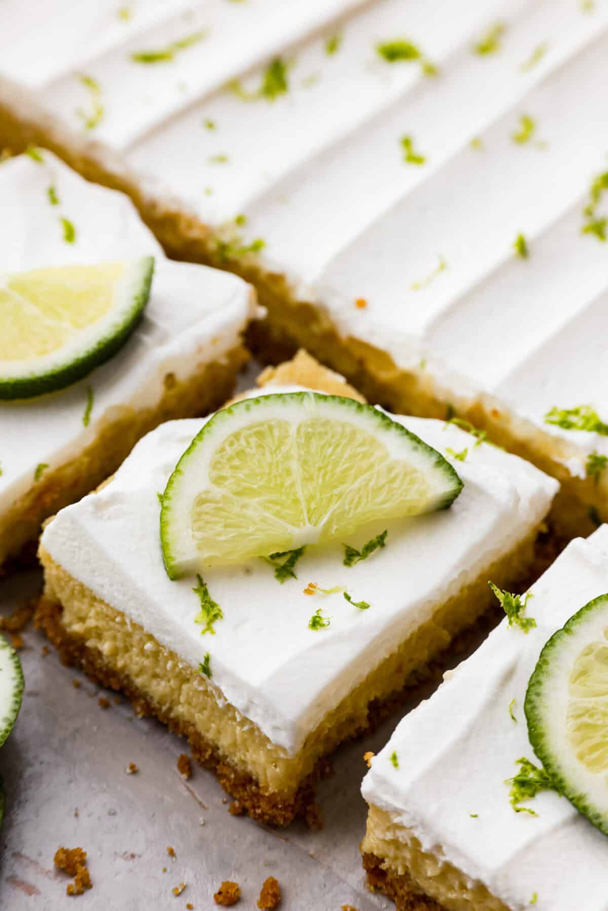 Key lime pie bars are classic key lime pie flavors baked into delightful little bars. They have a buttery graham cracker crust and a creamy lime filling. The sweet and zingy lime flavors make for an irresistible treat! Close view of key lime pie bars cut and garnished with lime slices and zest.