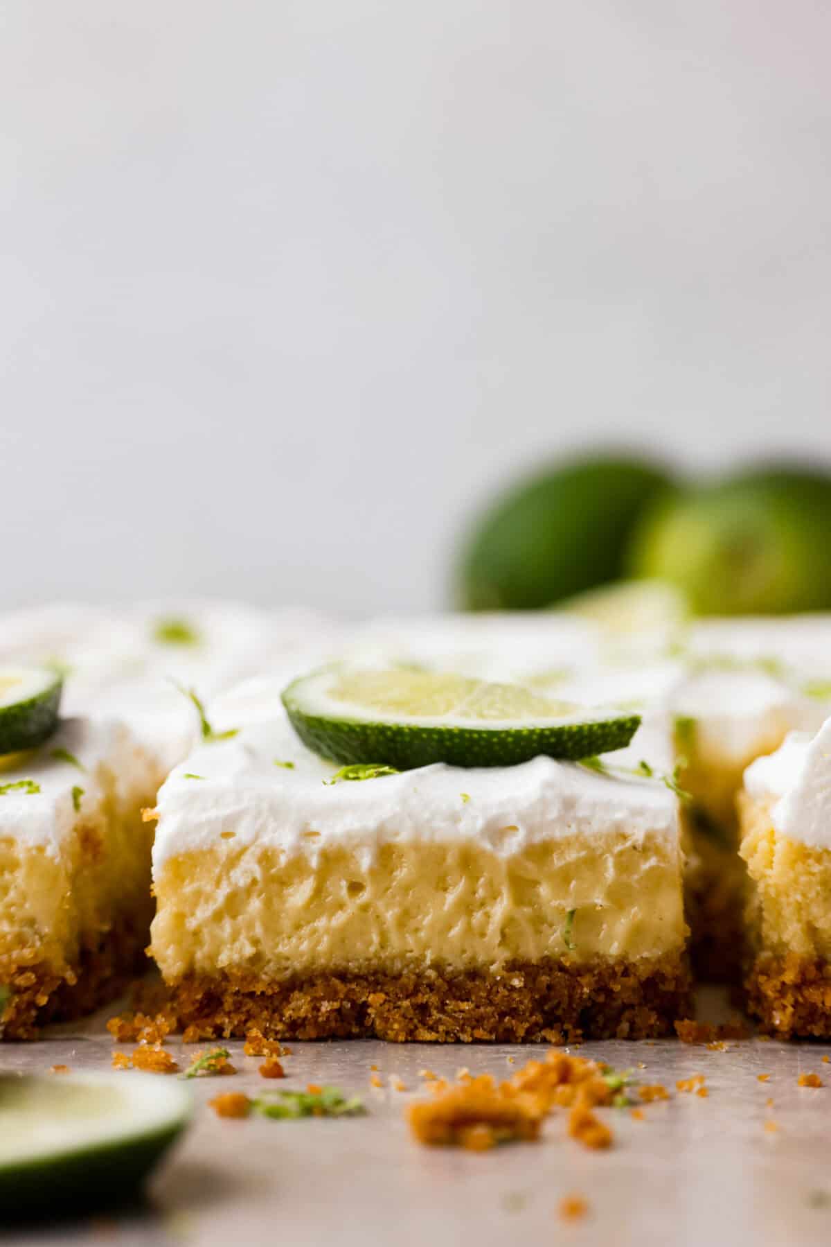 Key lime pie bars are classic key lime pie flavors baked into delightful little bars. They have a buttery graham cracker crust and a creamy lime filling. The sweet and zingy lime flavors make for an irresistible treat! Close side view of key lime pie bars.