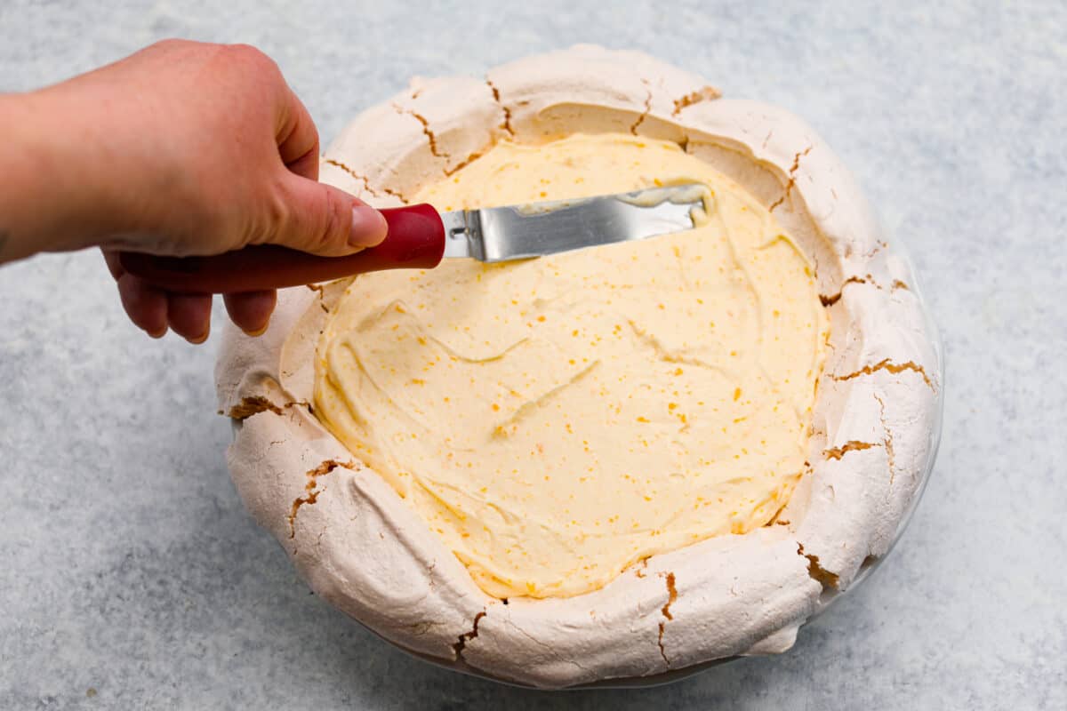 Lemon angel pie is a delightful dessert straight from heaven! It has a creamy lemon filling inside a sweet, airy meringue crust, then topped with fresh whipped cream. Every bite is pure bliss! Fifth process photo of the lemon filling being spread into the meringue pie shell.